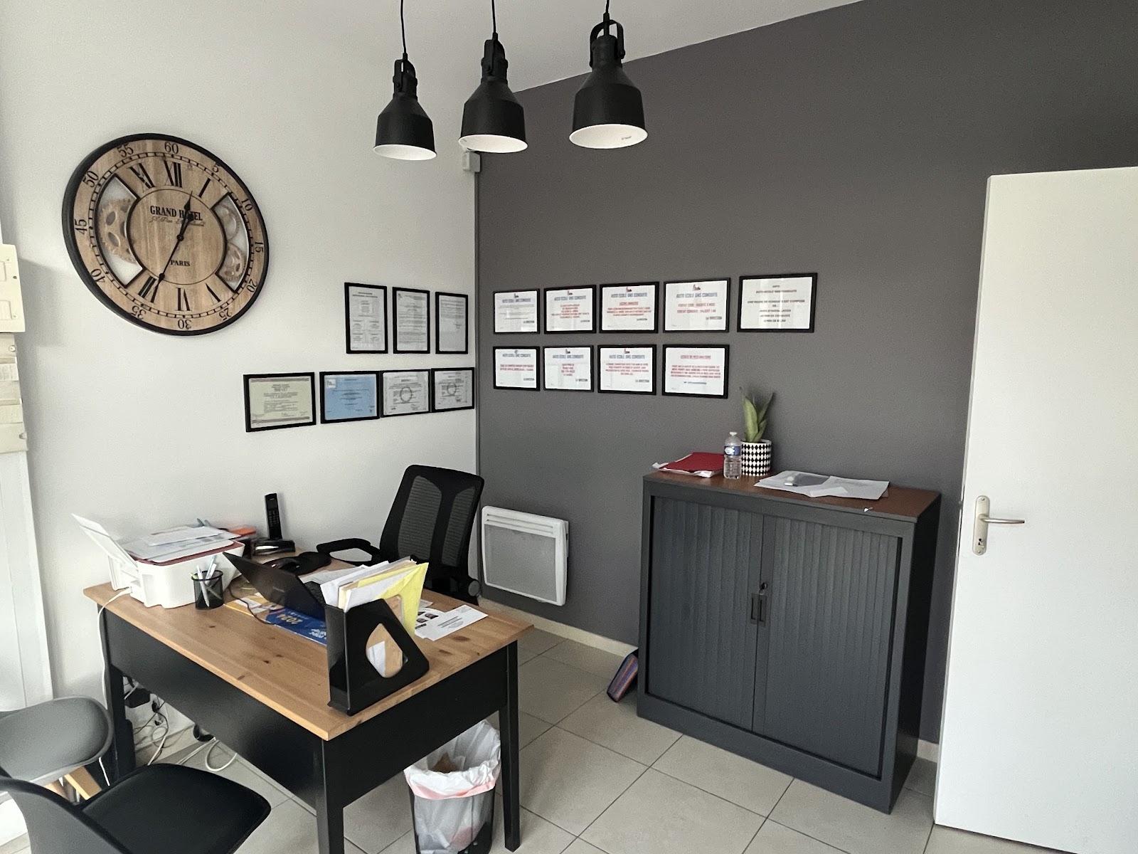 Le bureau de CFC Auto-École : table d'inscription, horloge, et les autorisations encadrées alignées sur le mur gris.