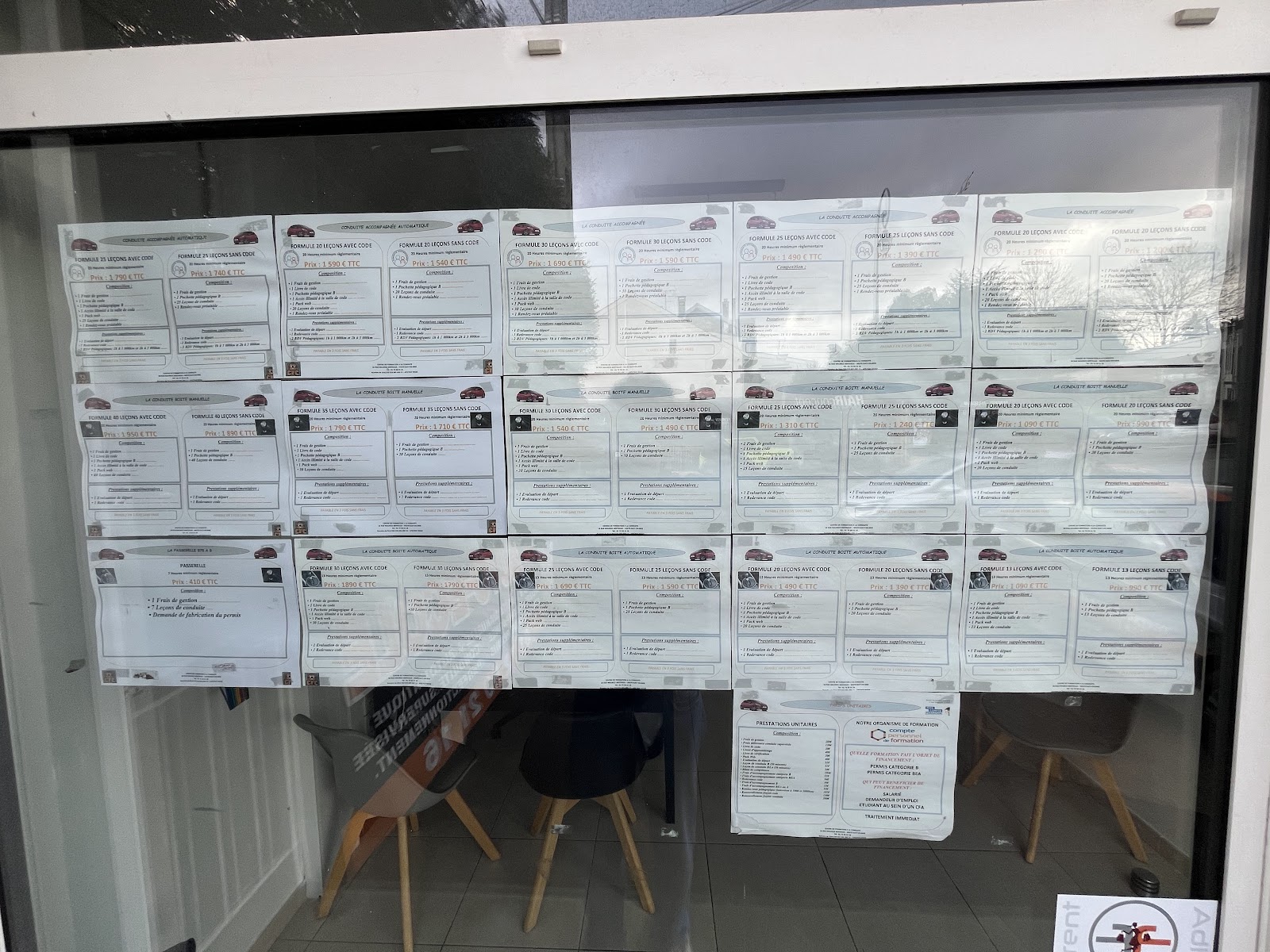 Le tableau des tarifs affiché en vitrine : une vingtaine de fiches de formules, conduite accompagnée, boîte manuelle, boîte automatique, passerelle et prestations unitaires.